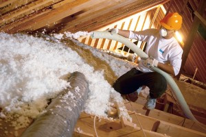 A technician installing loose-fill fiberglass insulation in an attic