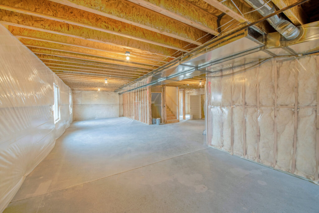 Large unfinished basement with woodframes and wall insulation. Basement interior with plastic vapor barrier and windows on the left side.
